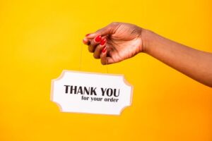A hand holding a thank you sign on a bright yellow background, expressing gratitude.