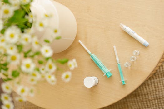 Top view of diabetic care kit with syringes and injector pen on a wooden table with flowers.