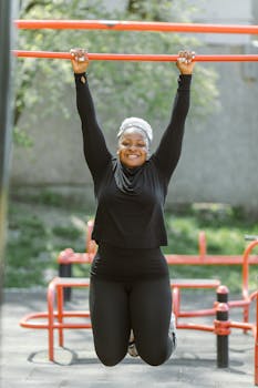 Smiling woman in sportswear enjoying an outdoor workout on monkey bars in a park.