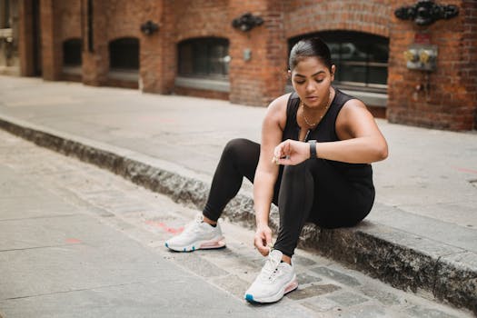 Woman in activewear checking smartwatch while sitting on urban sidewalk.
