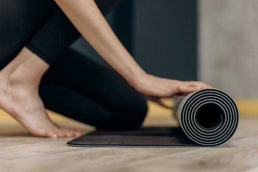 A woman rolls up a yoga mat on a wooden floor, signifying tranquility and mindfulness.