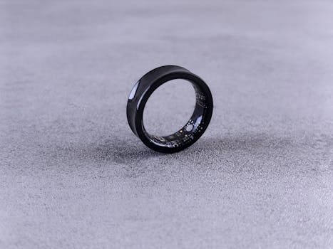 A modern black smart ring with visible circuitry resting on a textured concrete surface.