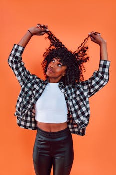 Confident woman in checkered jacket and curly hair posing against orange background.