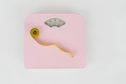 A pink weighing scale paired with a yellow measuring tape on a white backdrop.