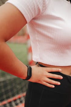 A close-up shot of a woman's torso in white crop top with a fitness tracker on her wrist outdoors.
