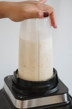 Close-up of a hand blending a smoothie in a sleek blender, highlighting food preparation.