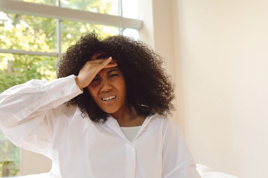 African American woman experiencing headache, holding forehead in discomfort indoors.
