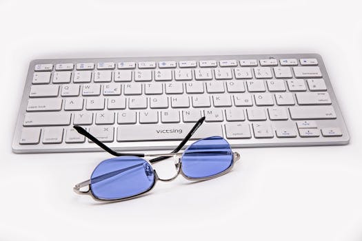 A wireless keyboard paired with blue light blocking glasses on a white surface, ideal for tech-related visuals.