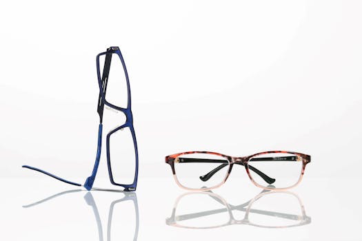 Modern eyeglasses in blue and a red pattern on a reflective white surface, showcasing style and elegance.