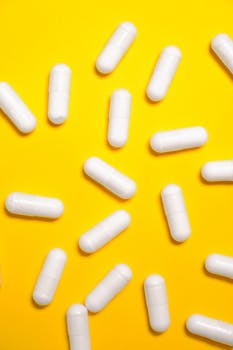 White capsules scattered on a vibrant yellow surface, symbolizing health and medicine.