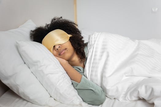 A woman with afro hair sleeps soundly in bed with a sleep mask, enjoying a cozy indoor atmosphere.