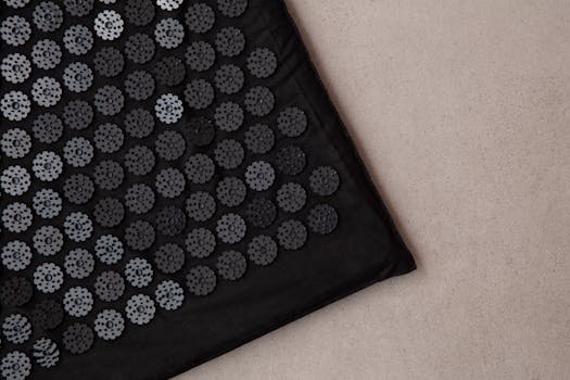 Detailed view of a black acupuncture mat on a neutral background, promoting relaxation and wellness.
