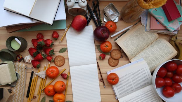 A top view of various fruits, books, and stationery creatively arranged on a wooden table.