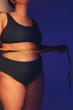 Plus-size woman measuring waist with tape measure in studio lighting.