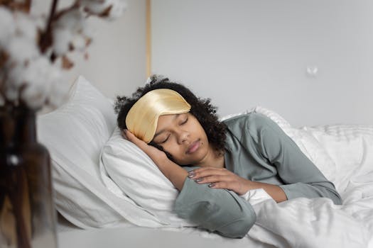A young woman peacefully sleeps with a sleep mask, nestled in cozy white bedding.