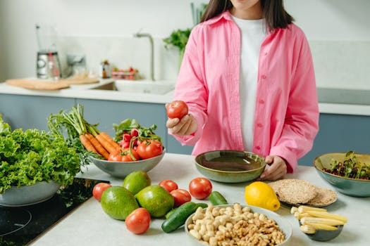Woman in pink overshirt holds tomato in kitchen with fresh fruits and veggies.
