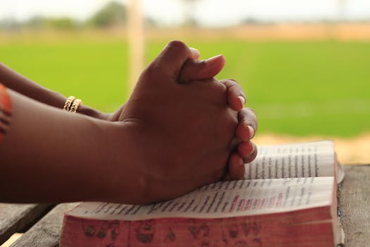 Close-up of hands clasped in prayer over an open Bible, symbolizing faith and devotion.