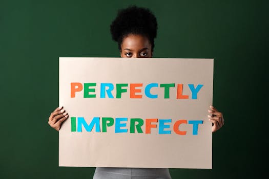 African woman holding a 'Perfectly Imperfect' sign, green background.