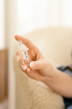A close-up of a hand with manicured nails holding a clear medical ampoule, suitable for healthcare imagery.