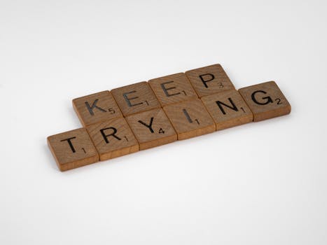 Scrabble tiles form an inspiring message 'Keep Trying' on a white background. Motivational and clean aesthetic.