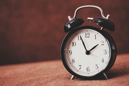 Close-up of a vintage black alarm clock showing twelve o'clock against a brown backdrop.