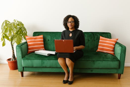 African American woman sitting on a green couch with a laptop, working from home.
