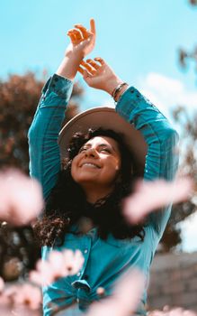 Woman with long hair and hat outdoors in spring, smiling and embracing nature.