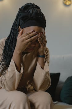 An African American woman with hands on face, appearing troubled and sitting indoors.