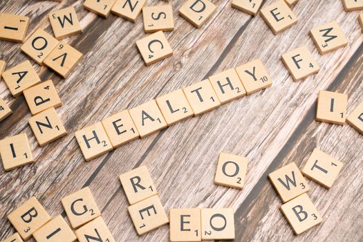 Wooden letter tiles arranged on a wooden surface spelling out 'healthy', symbolizing wellness.
