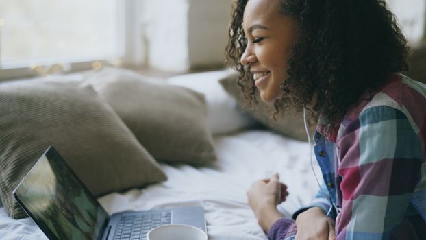 Smiling young woman using a laptop in a cozy indoor setting, enjoying online interaction.