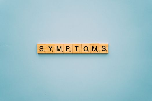 Scrabble tiles spelling 'SYMPTOMS' on a blue background, symbolizing health concepts.