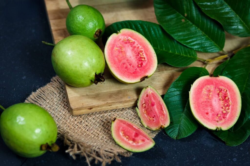 Vibrant fresh guavas sliced with leaves on a wooden board, showcasing tropical fruit freshness.
