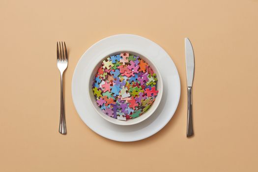 A conceptual still life of colorful puzzle pieces in a bowl, styled as a meal setting.