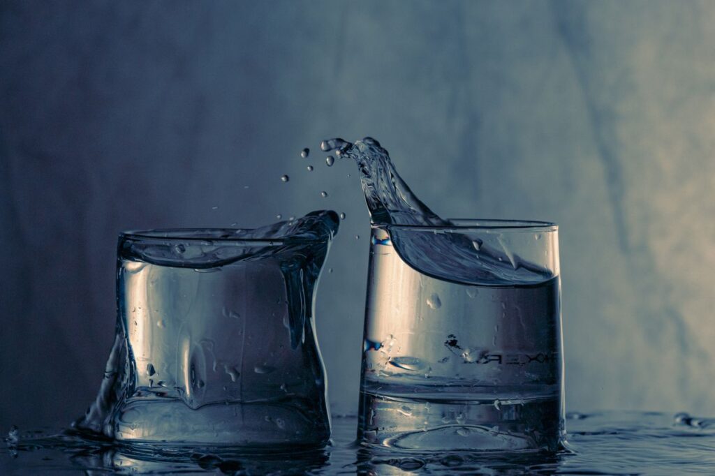 Close-up of splashing water between two glasses on a blue background.