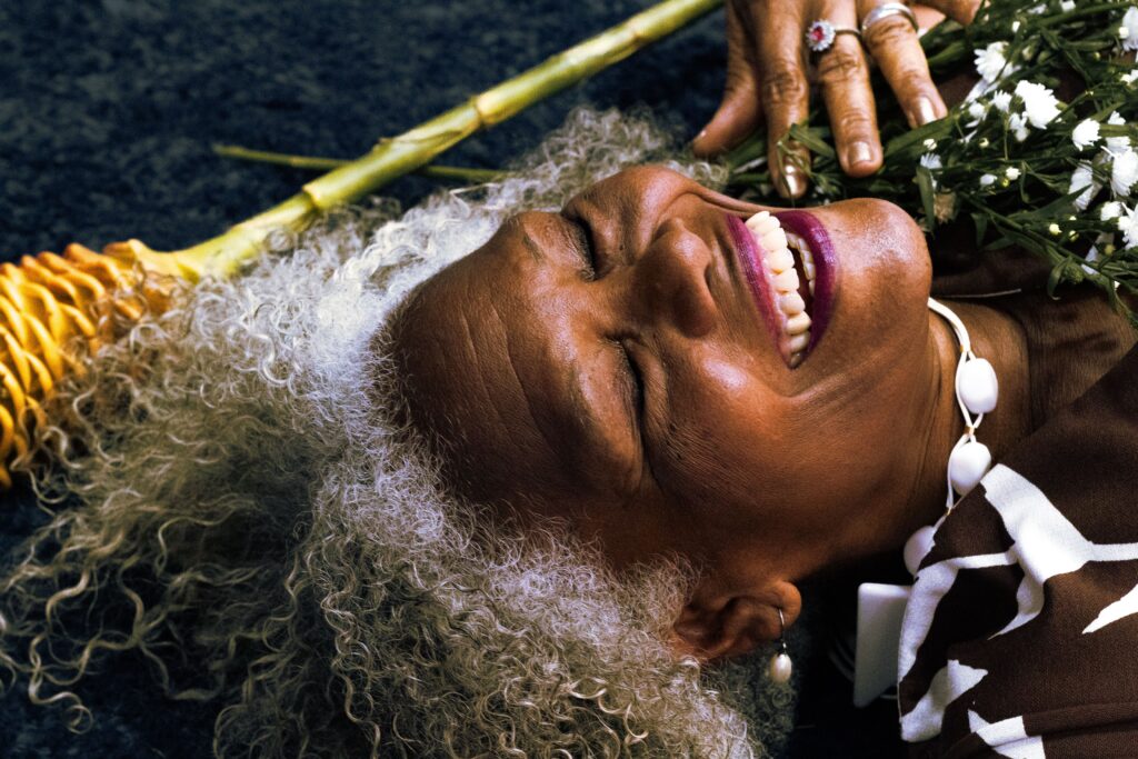 Smiling senior woman resting with flowers, embracing joy and nature's beauty.