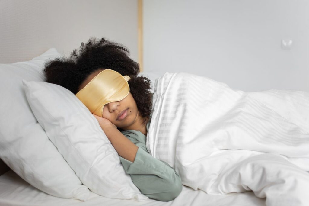 A woman peacefully sleeping with an eye mask in a cozy white bedroom setting.
