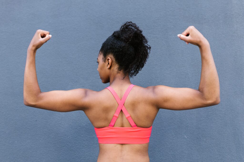 Rear view of a fit woman flexing muscles in a pink sports bra against a gray background.