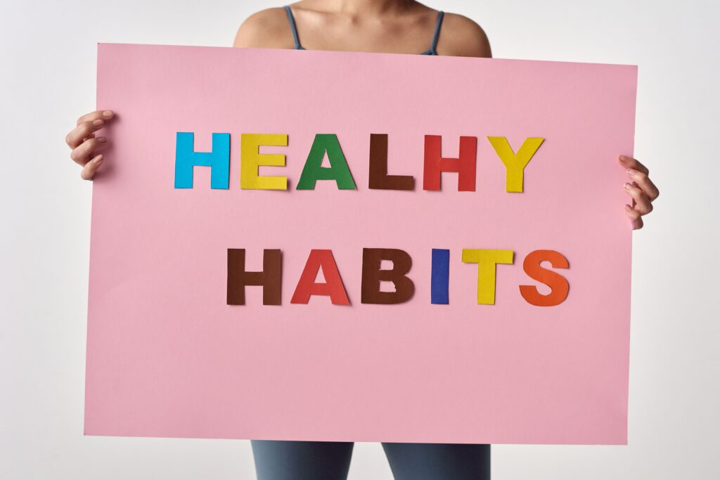 A woman holds a pink poster with colorful letters spelling 'HEALTHY HABITS'.