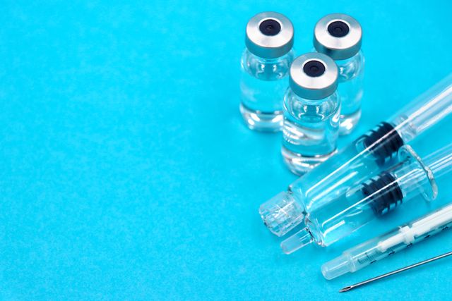 Close-up of vaccine vials and syringes on a blue surface, emphasizing healthcare.