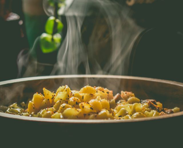 Big round bowl with aromatic pasta with herbs and vegetables smoking in soft light as a prepared meal for work to place in cordless heated lunch box