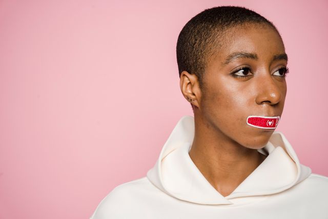 African American woman with Band-Aid / tape on lips, on a pink background, showing mouth taping