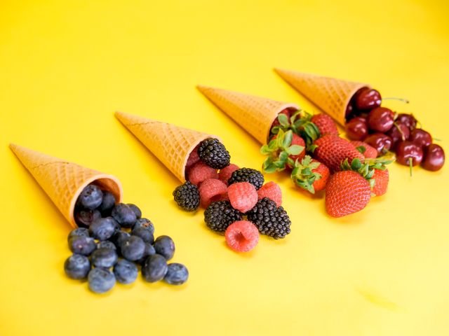Vibrant assortment of berries in waffle cones on a bright yellow surface.